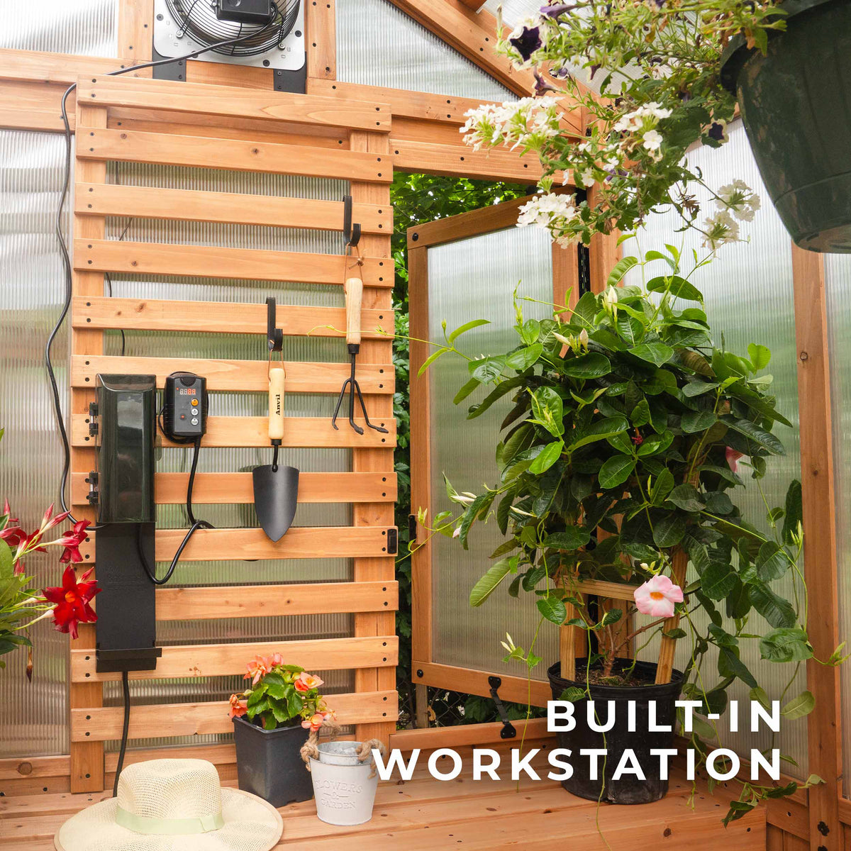 Slat wall workstation inside a cedar greenhouse displaying hanging garden tools and a mounted thermostat.