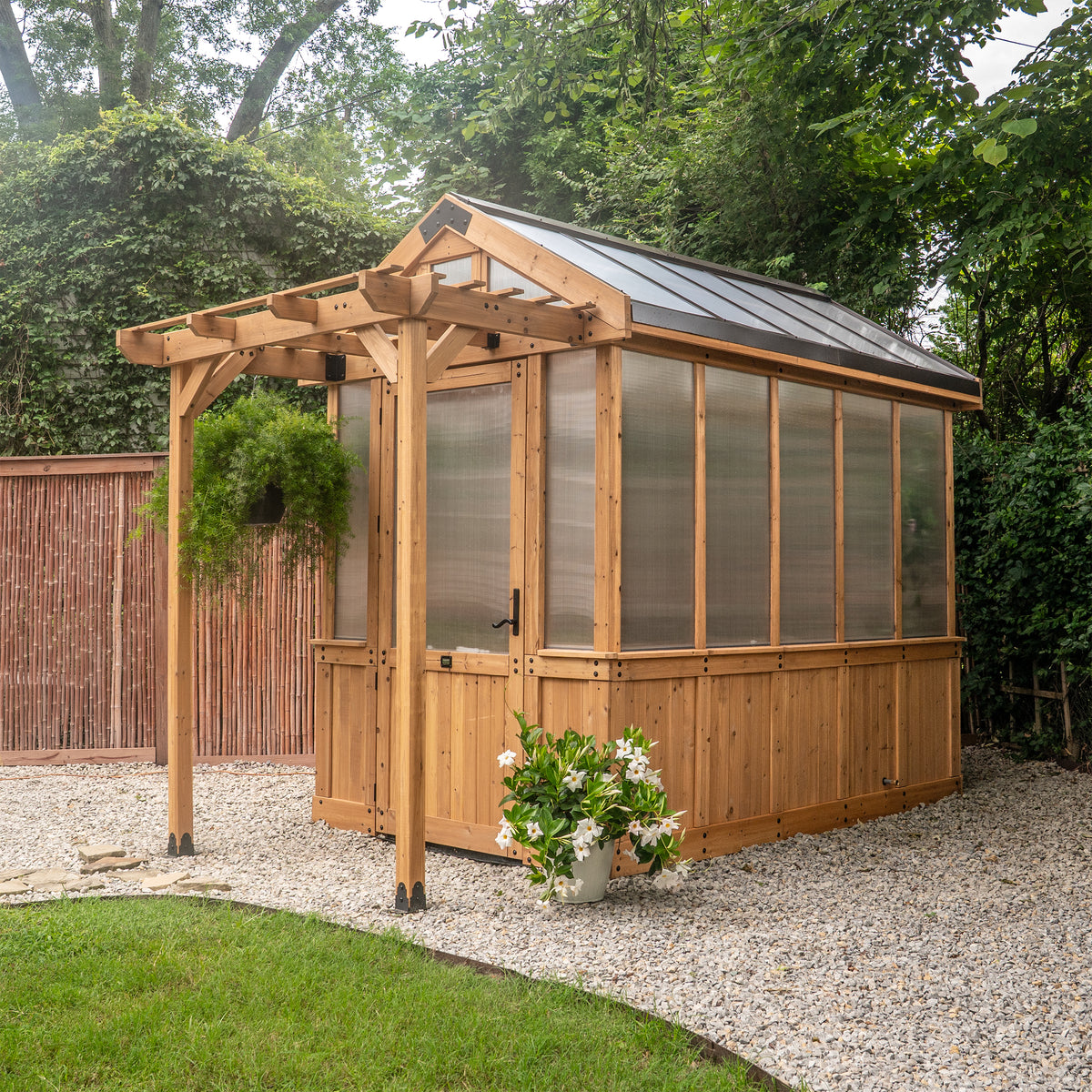 Cedar greenhouse kit with 4-wall polycarbonate panels and a peaked roof in a gravel backyard.