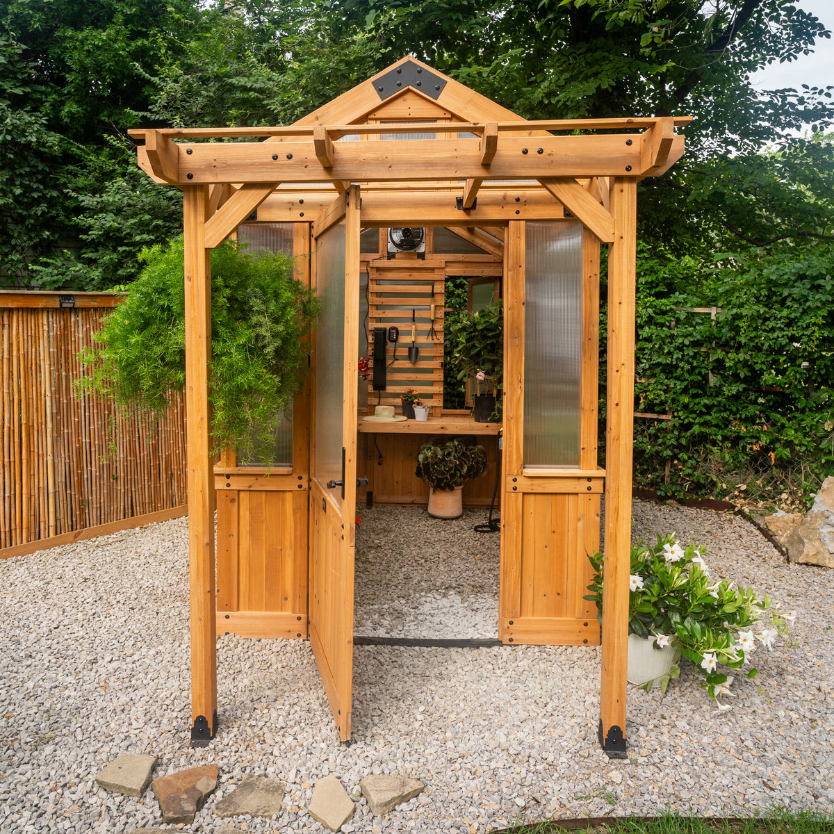4-wall polycarbonate greenhouse with open wide entry door revealing an organized interior with tools and plants.